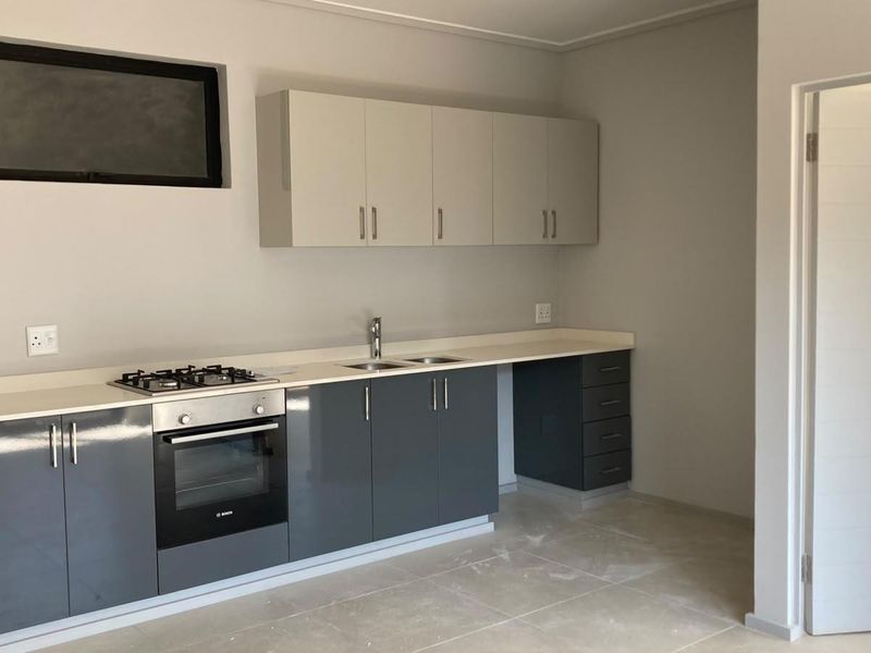 Modern kitchen featuring sleek grey and white cabinetry, stone countertops, integrated gas hob, electric oven, and tiled flooring in a clean, minimalist space.
