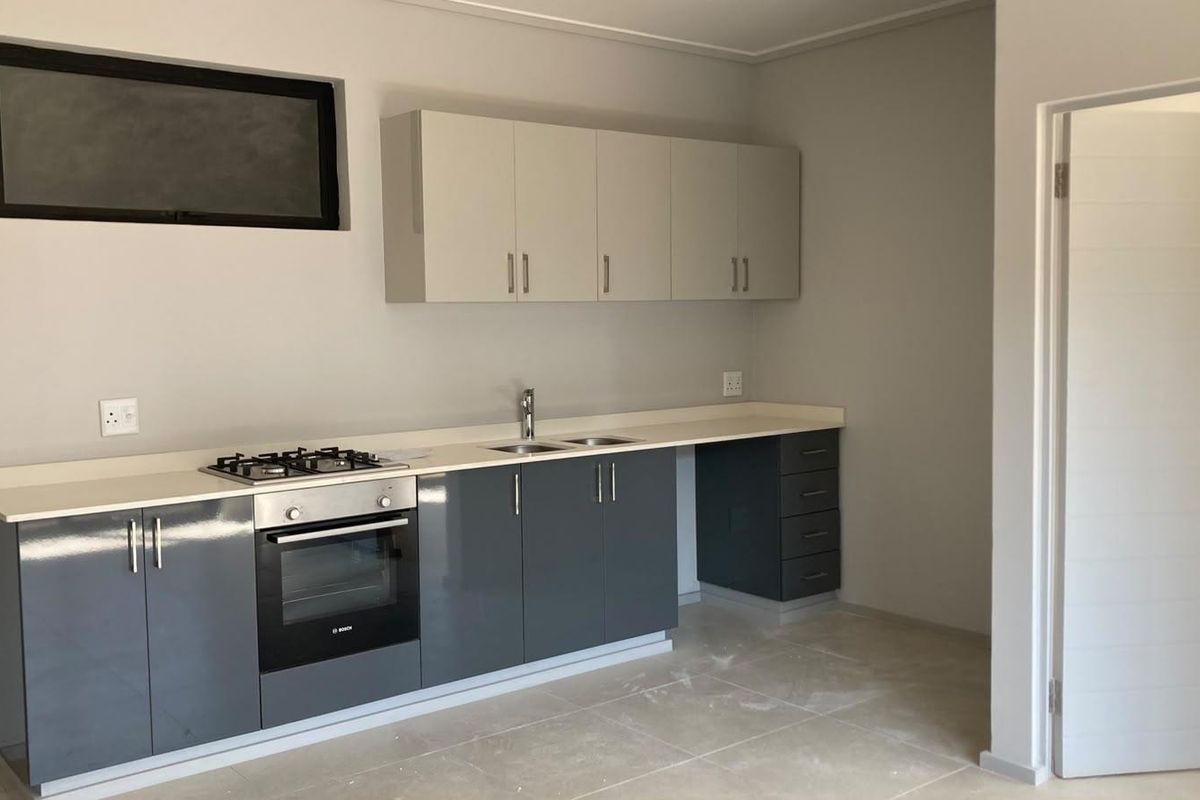 Modern kitchen featuring sleek grey and white cabinetry, stone countertops, integrated gas hob, electric oven, and tiled flooring in a clean, minimalist space.