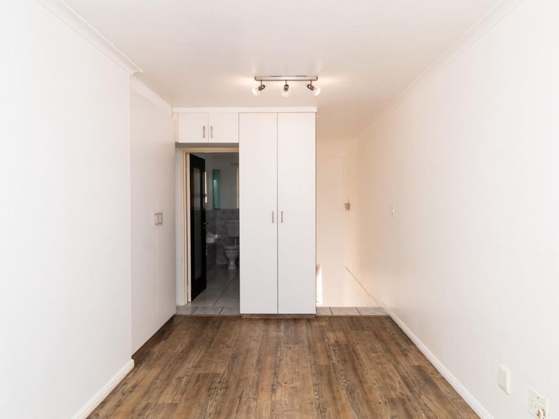 An empty bedroom featuring laminate flooring, built-in cupboards, and a ceiling-mounted spotlight, with an adjacent view into a bathroom.