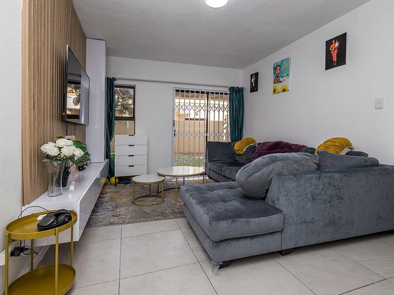 A well-maintained living room featuring tiled flooring, a modern feature wall with a built-in media console, and sliding glass doors leading to the exterior.