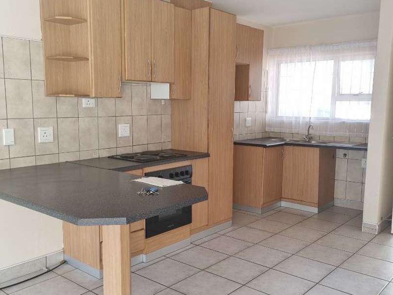 A functional kitchen featuring light wood-look laminate cabinetry, a built-in oven with electric hob, tiled backsplash, and neutral floor tiles.