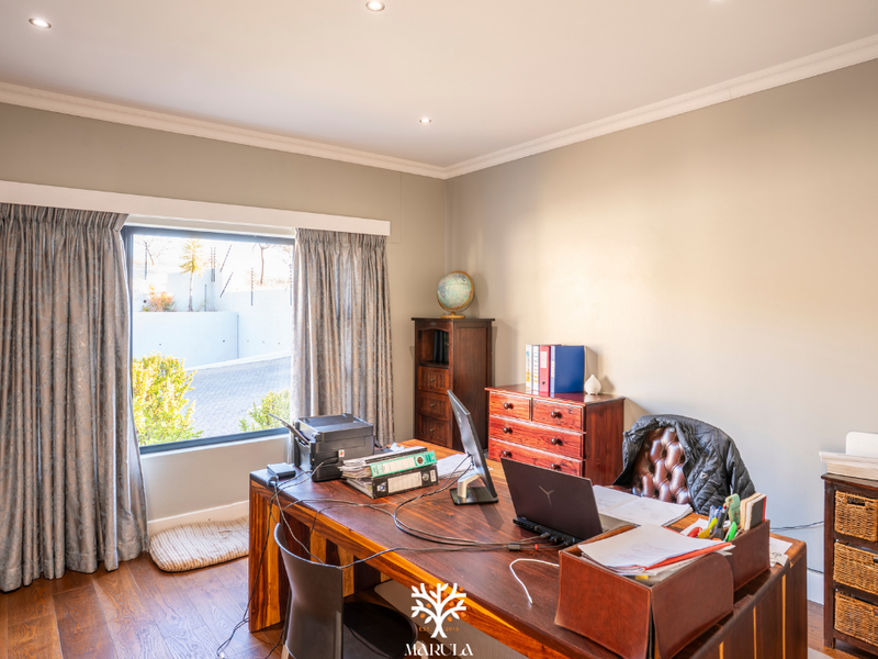 A well-lit home office featuring hardwood flooring, recessed downlights, and a large window providing natural light.