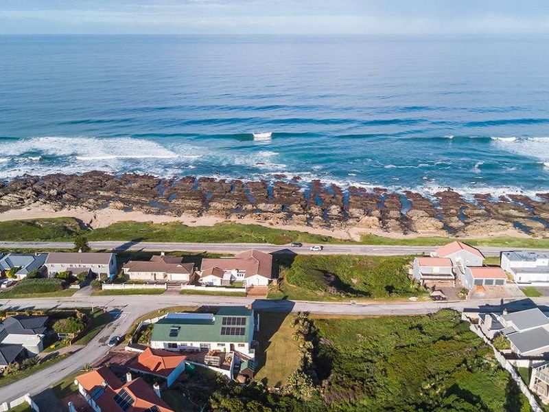 Aerial view of a coastal residential neighborhood featuring homes with solar panels, situated directly along the rocky shoreline and ocean.