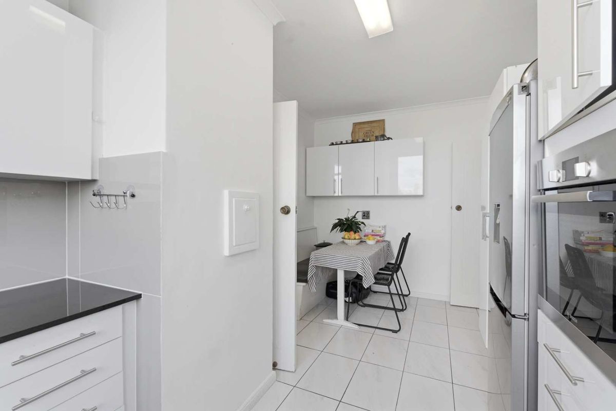 A modern, compact kitchen featuring gloss white cabinetry, black stone countertops, and clean tiled flooring, offering a functional and bright workspace.