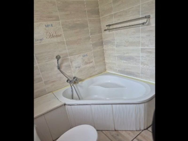 A bathroom featuring a corner bathtub with a handheld shower mixer, tiled walls, and a built-in vanity cabinet.
