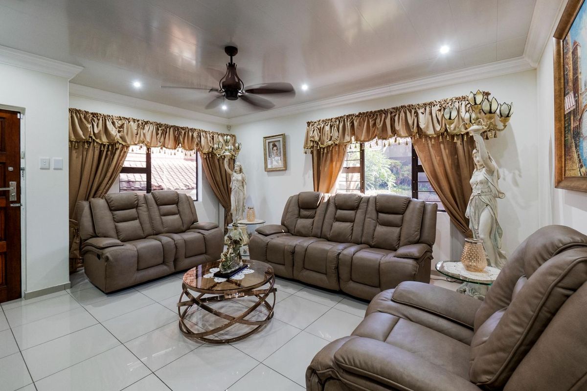 A spacious living room featuring polished floor tiles, a ceiling fan, and large windows with decorative pelmets.