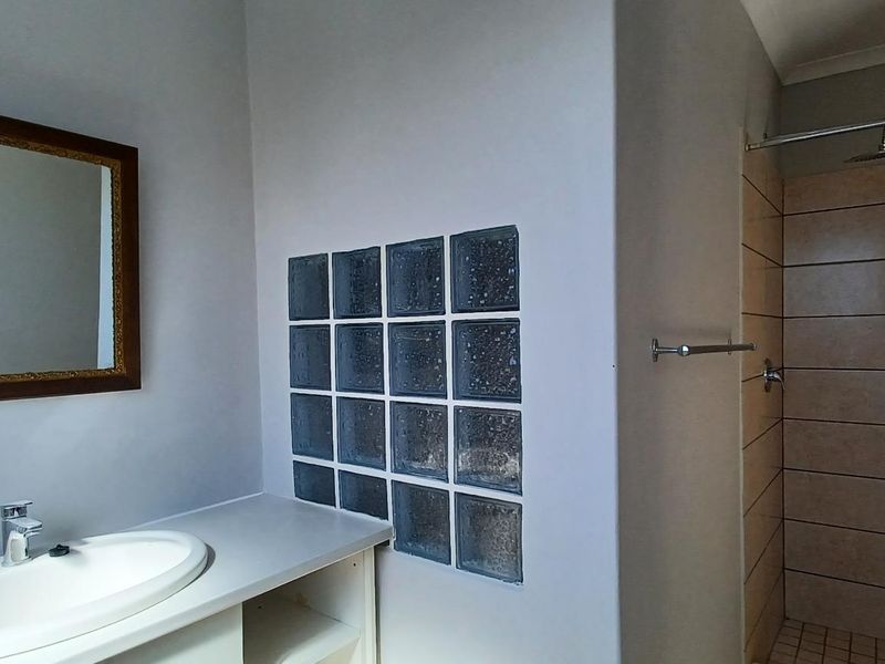 A functional bathroom featuring a vanity with integrated basin, a glass block feature wall, and a tiled shower enclosure.