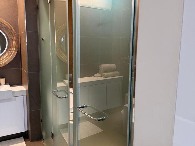 Modern bathroom featuring a frosted glass shower enclosure, vanity cabinet with basin, and neutral tiled finishes.