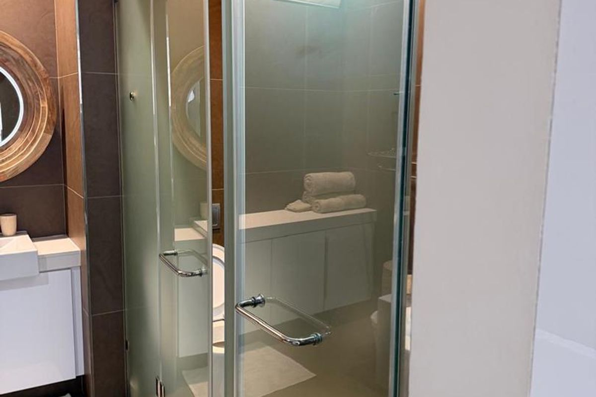 Modern bathroom featuring a frosted glass shower enclosure, vanity cabinet with basin, and neutral tiled finishes.