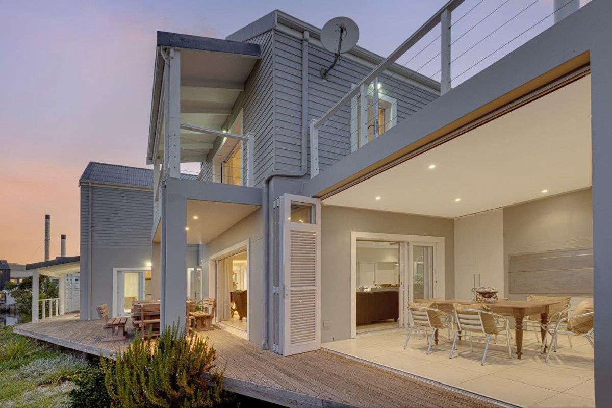 A modern two-story home featuring a spacious covered patio, timber decking, and seamless indoor-outdoor flow through large sliding doors.