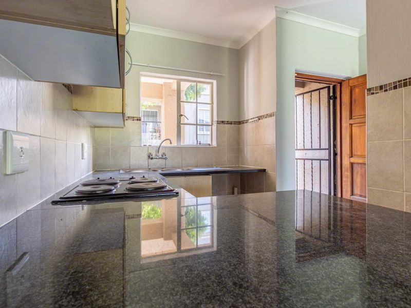 A functional kitchen featuring granite countertops, an electric hob, tiled backsplash, and a stainless steel sink, with direct access to an exterior security gate.