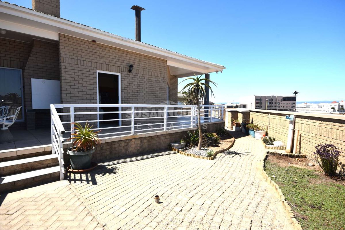 A rear exterior view of the townhouse featuring a paved patio area, white metal railings, and a brick facade with a chimney stack.