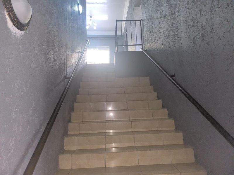 A functional interior staircase featuring tiled steps, metal handrails, and textured grey walls leading to an upper landing.