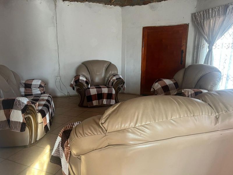 A living room area featuring tiled flooring and a wooden door, currently requiring significant maintenance and cosmetic updates to the walls and ceiling.