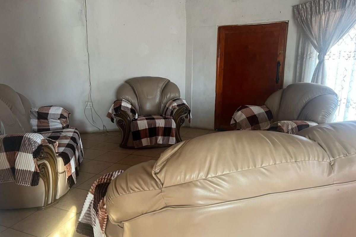 A living room area featuring tiled flooring and a wooden door, currently requiring significant maintenance and cosmetic updates to the walls and ceiling.