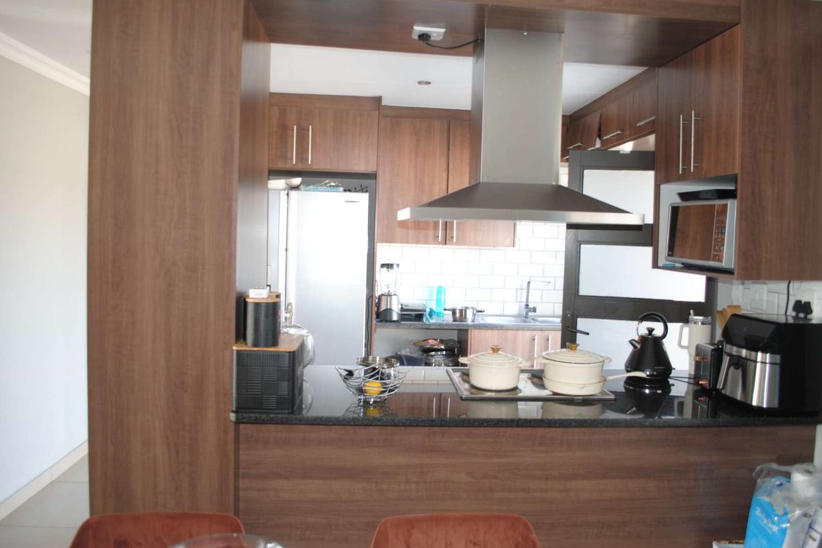 A functional kitchen featuring dark wood cabinetry, granite countertops, a built-in hob, and a stainless steel extractor fan.