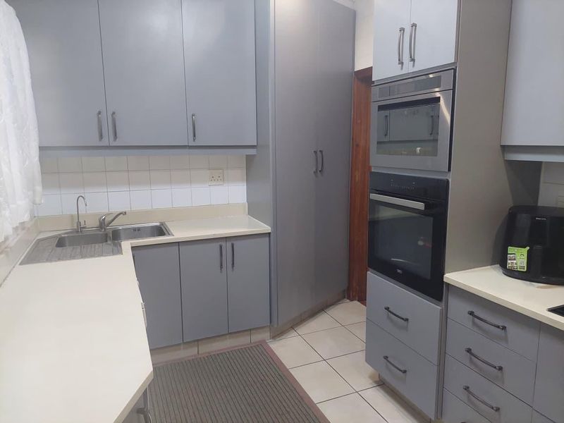 A modern kitchen featuring grey cabinetry, integrated oven and microwave, tiled splashback, and a stainless steel sink with ample counter space.
