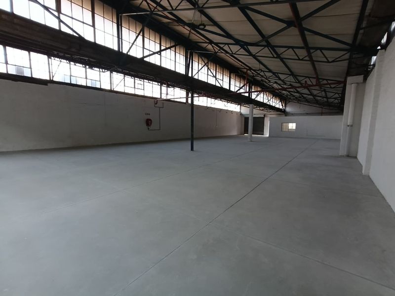 Spacious industrial warehouse unit featuring high ceilings with exposed steel trusses, large clerestory windows for natural light, and durable concrete flooring.