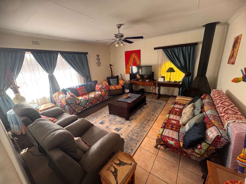 Spacious living room featuring tiled flooring, a ceiling fan, and a freestanding fireplace, offering a comfortable and functional family space.