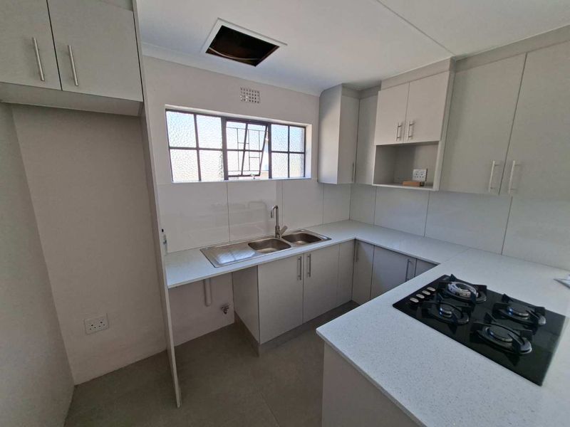 A clean, modern kitchen featuring light grey cabinetry, stone countertops, a gas hob, and a stainless steel double sink with a tiled splashback.
