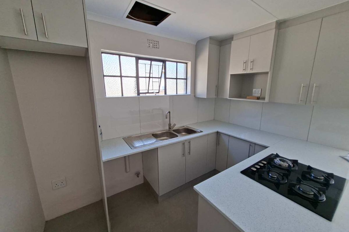 A clean, modern kitchen featuring light grey cabinetry, stone countertops, a gas hob, and a stainless steel double sink with a tiled splashback.