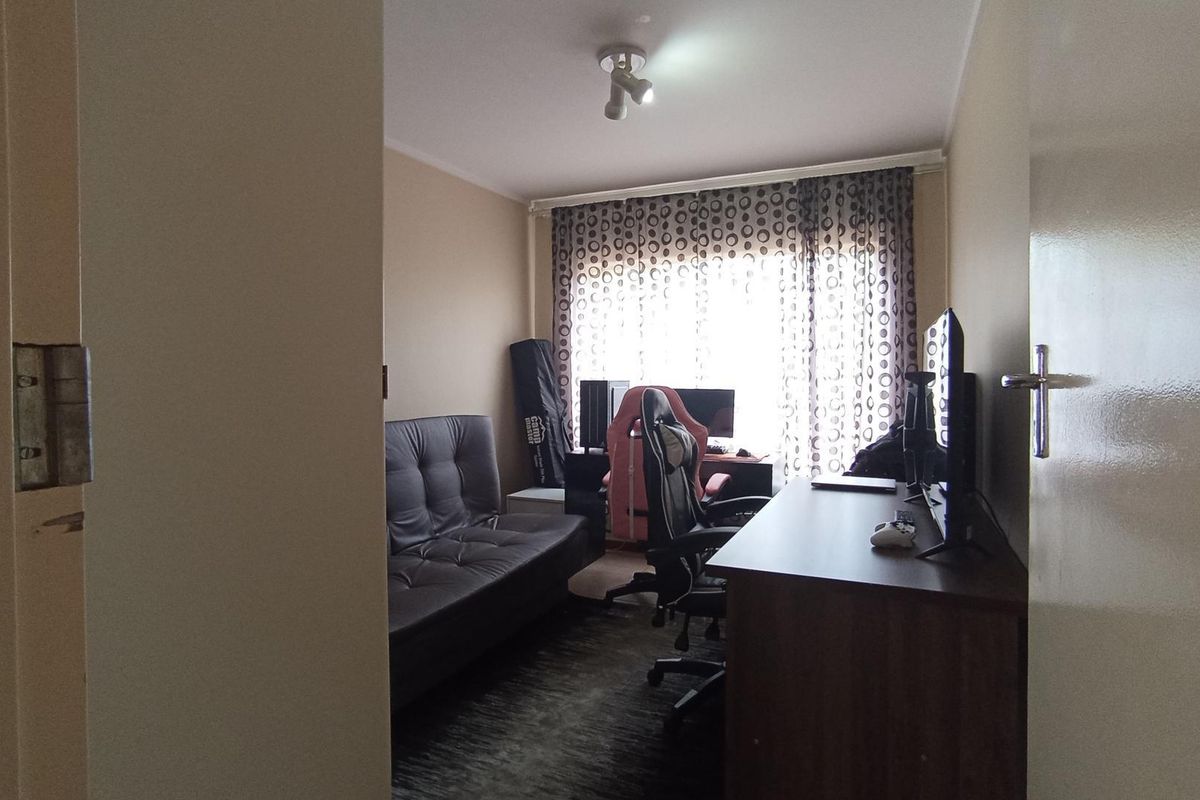 A functional bedroom or home office space featuring a window with curtains and overhead lighting.