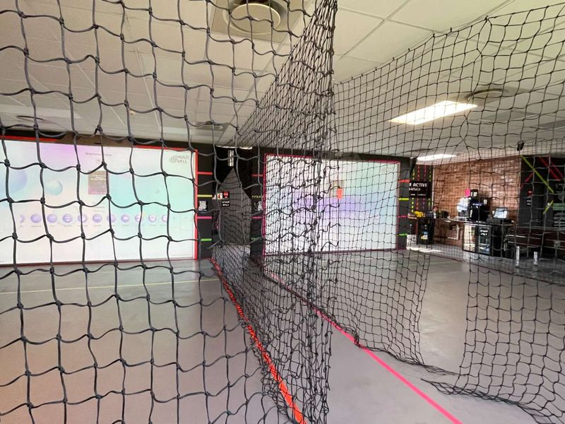 A modern indoor sports facility featuring interactive projection screens, safety netting, and durable vinyl flooring, suitable for active gaming or training.