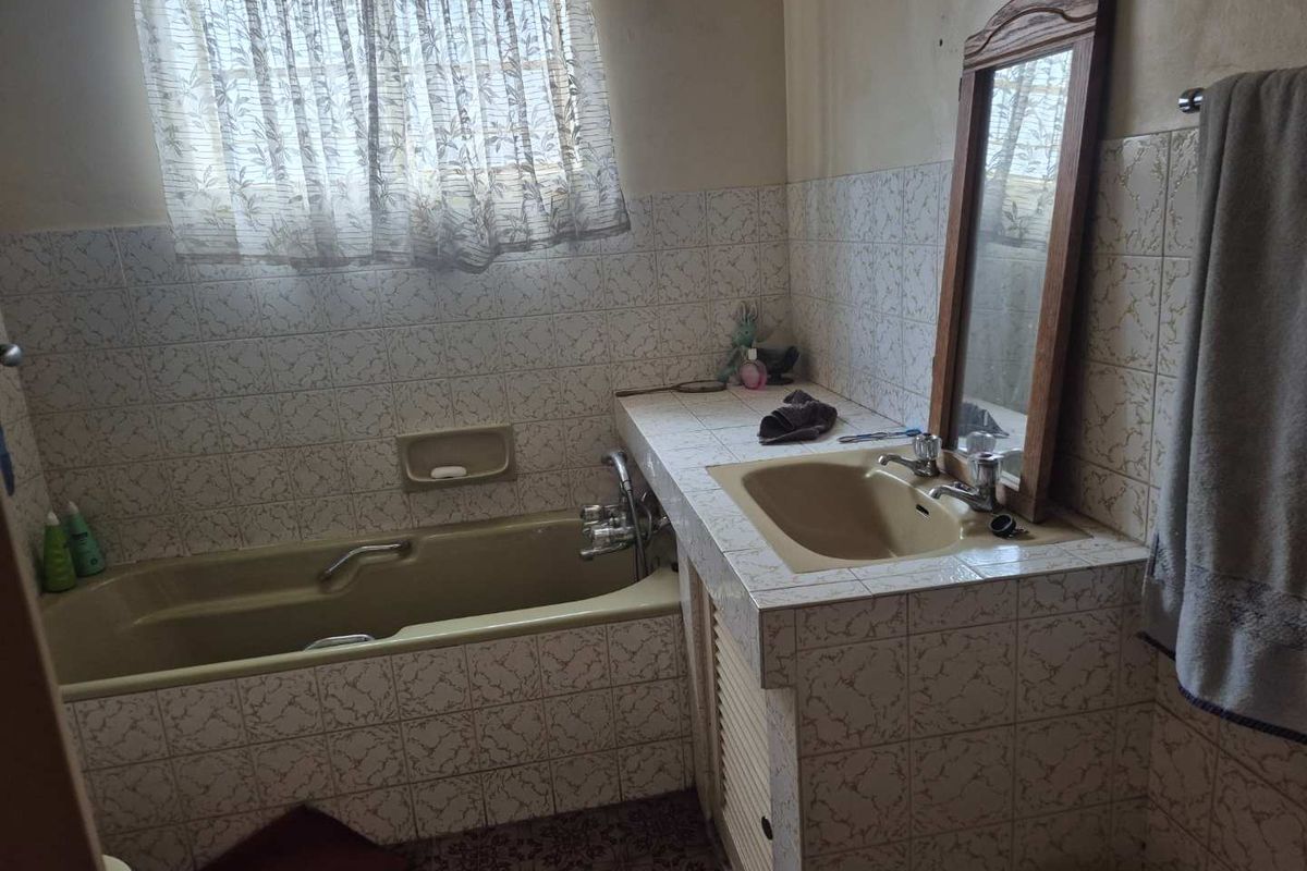 A dated bathroom featuring a built-in bathtub and vanity unit with tiled surfaces, requiring modernization to improve aesthetic appeal and functionality.