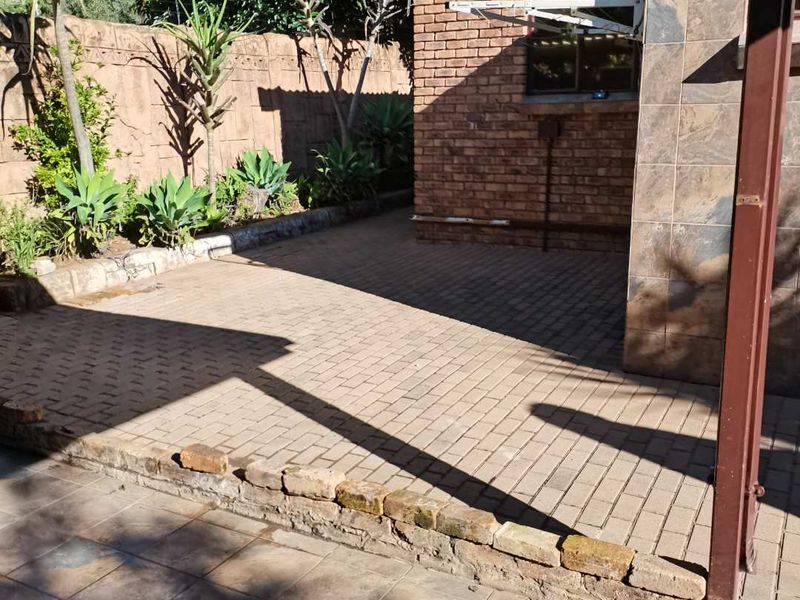 A paved rear courtyard area featuring a brick exterior wall, tiled facade accents, and a low retaining wall border.