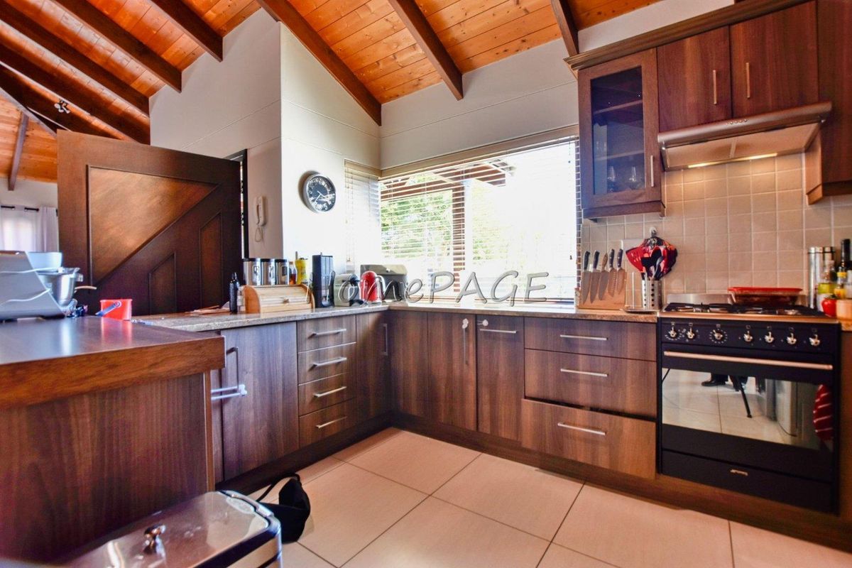 A functional kitchen featuring dark wood cabinetry, tiled flooring, a built-in oven with gas hob, and a vaulted timber ceiling.