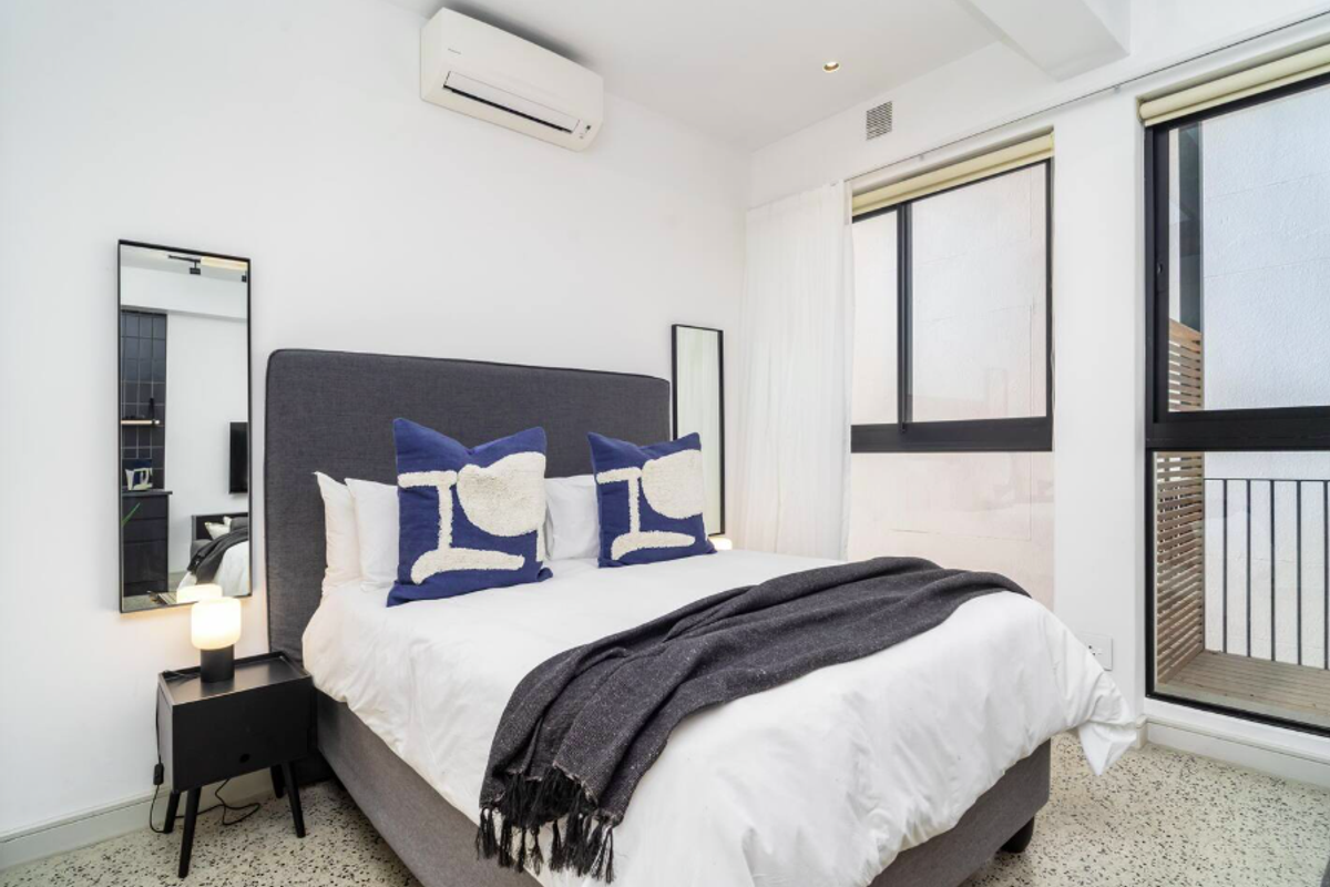 A bright bedroom featuring a wall-mounted air conditioning unit, large windows, and access to a private balcony with modern finishes.