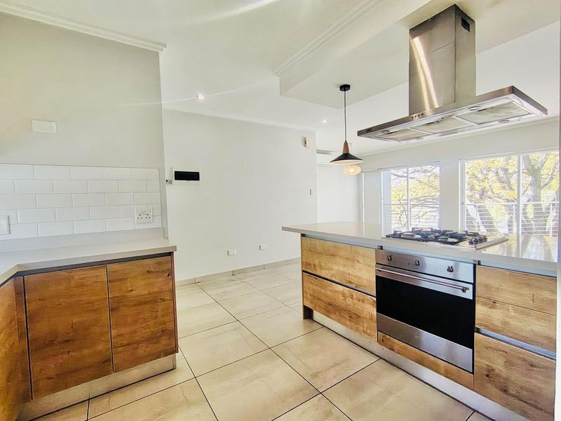 Modern kitchen featuring wood-finish cabinetry, stone countertops, subway tile backsplash, and integrated stainless steel appliances, including a gas hob and extractor fan.