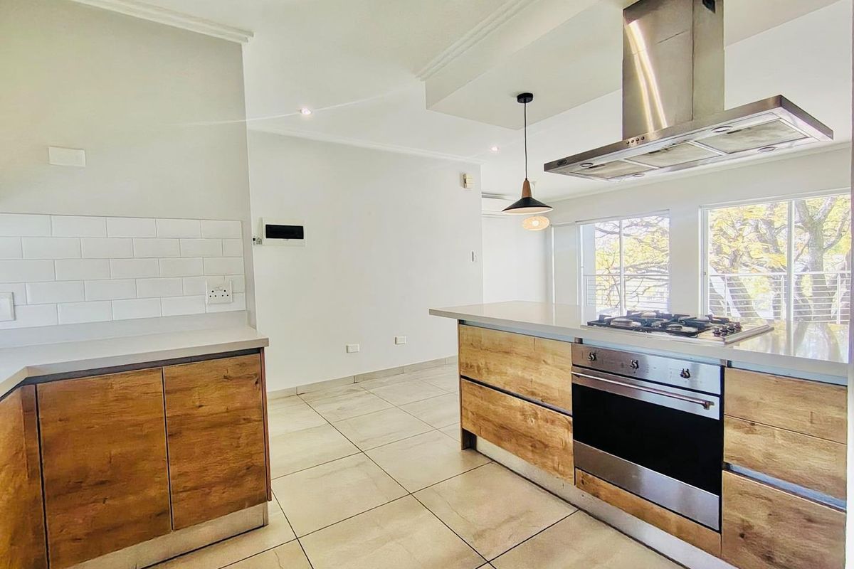 Modern kitchen featuring wood-finish cabinetry, stone countertops, subway tile backsplash, and integrated stainless steel appliances, including a gas hob and extractor fan.