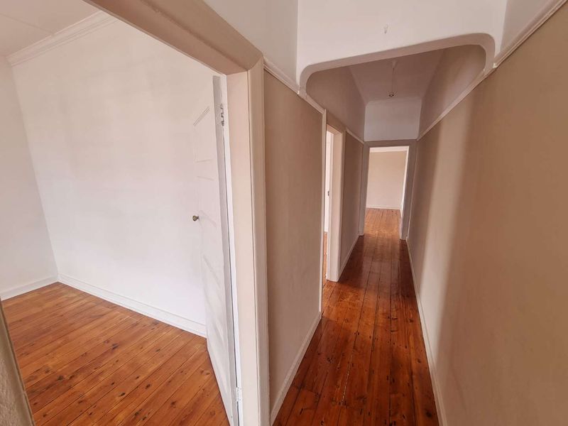 A bright, empty hallway featuring polished hardwood flooring, coved ceilings, and neutral wall finishes, providing access to adjacent rooms.