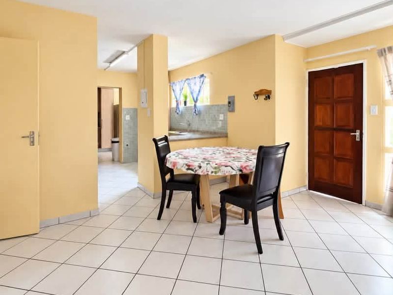 Open plan living and dining area featuring tiled flooring, a solid wood entrance door, and a view into the adjacent kitchen space.