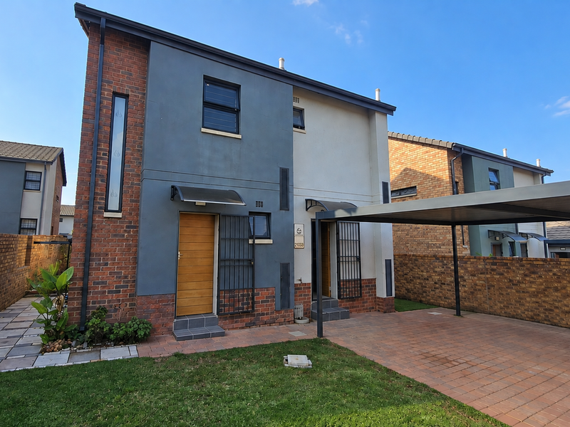 Modern two-story townhouse featuring a combination of brick and plastered finishes, a private carport, and a paved driveway with a small front garden.