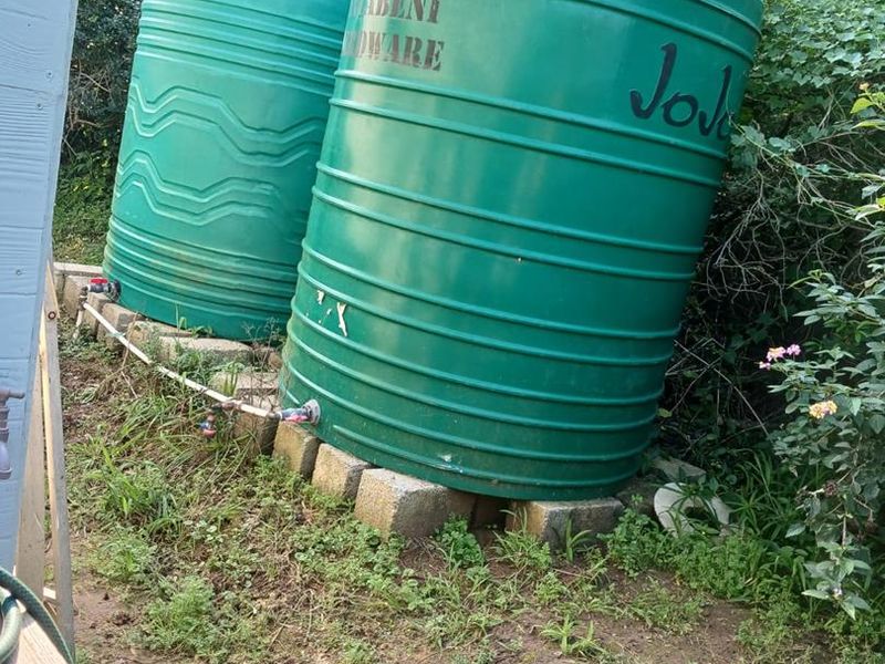 Two green plastic water storage tanks installed on a concrete block base in the garden area.