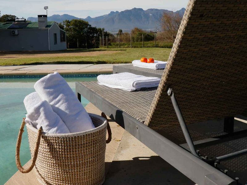 A serene pool area featuring a paved deck with mountain views and a cottage in the background.