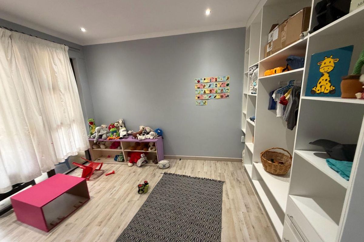 A bright bedroom featuring light wood-look flooring, recessed ceiling lighting, and extensive floor-to-ceiling built-in shelving units for storage.