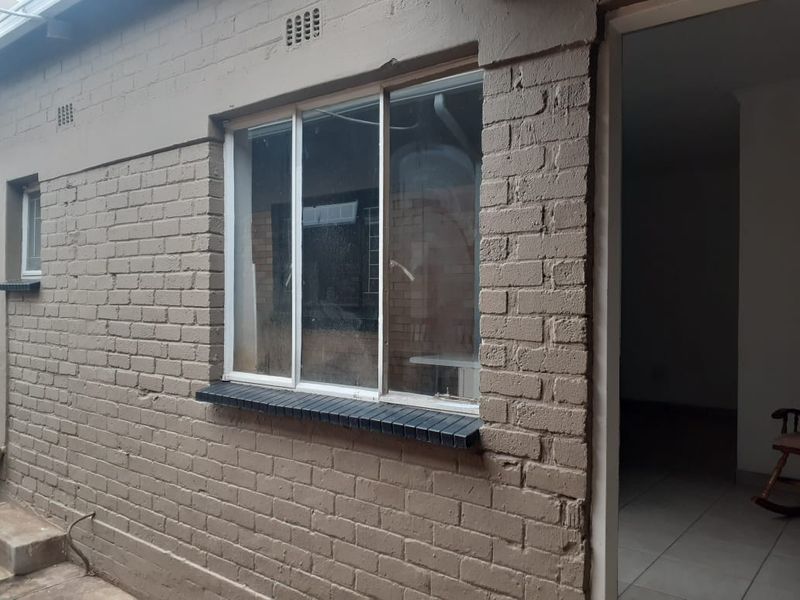 Exterior view of the cottage rear facade featuring painted brickwork and a sliding aluminium window with a brick sill.