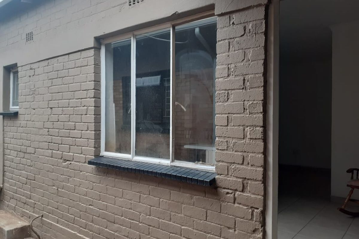 Exterior view of the cottage rear facade featuring painted brickwork and a sliding aluminium window with a brick sill.