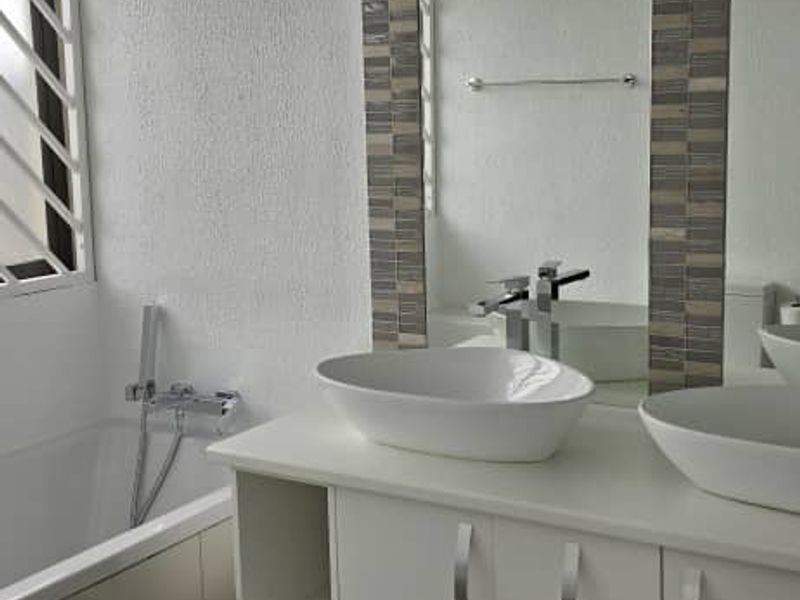 Modern bathroom featuring a double vanity with vessel sinks, a built-in bathtub, and large wall-mounted mirror with decorative tile accents.