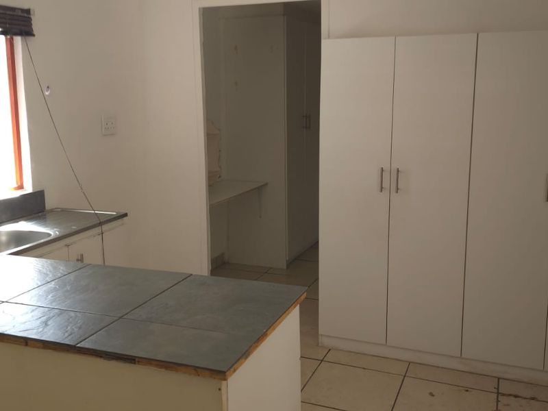 A functional kitchen area featuring built-in white cabinetry, a tiled countertop with an integrated sink, and tiled flooring throughout.