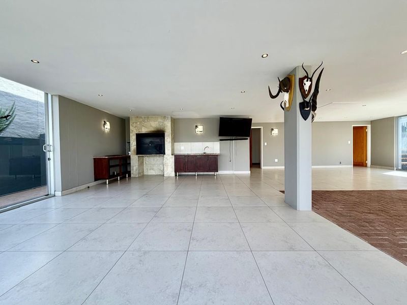 Spacious open-plan living area featuring large format floor tiles, a built-in fireplace, and integrated cabinetry with a sink, opening to an outdoor space.