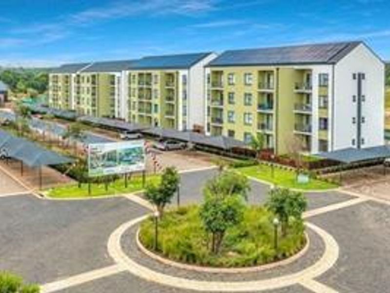 A wide-angle view of a modern apartment complex featuring paved driveways, covered parking bays, and well-maintained landscaped garden areas.