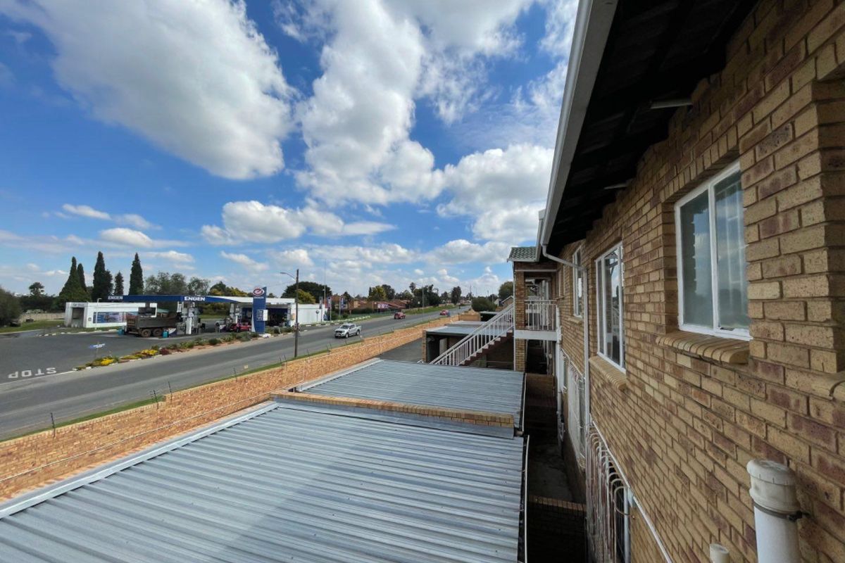 Exterior view of the apartment building showing face brick facade, corrugated metal roofing, and security bars, overlooking a nearby service station.