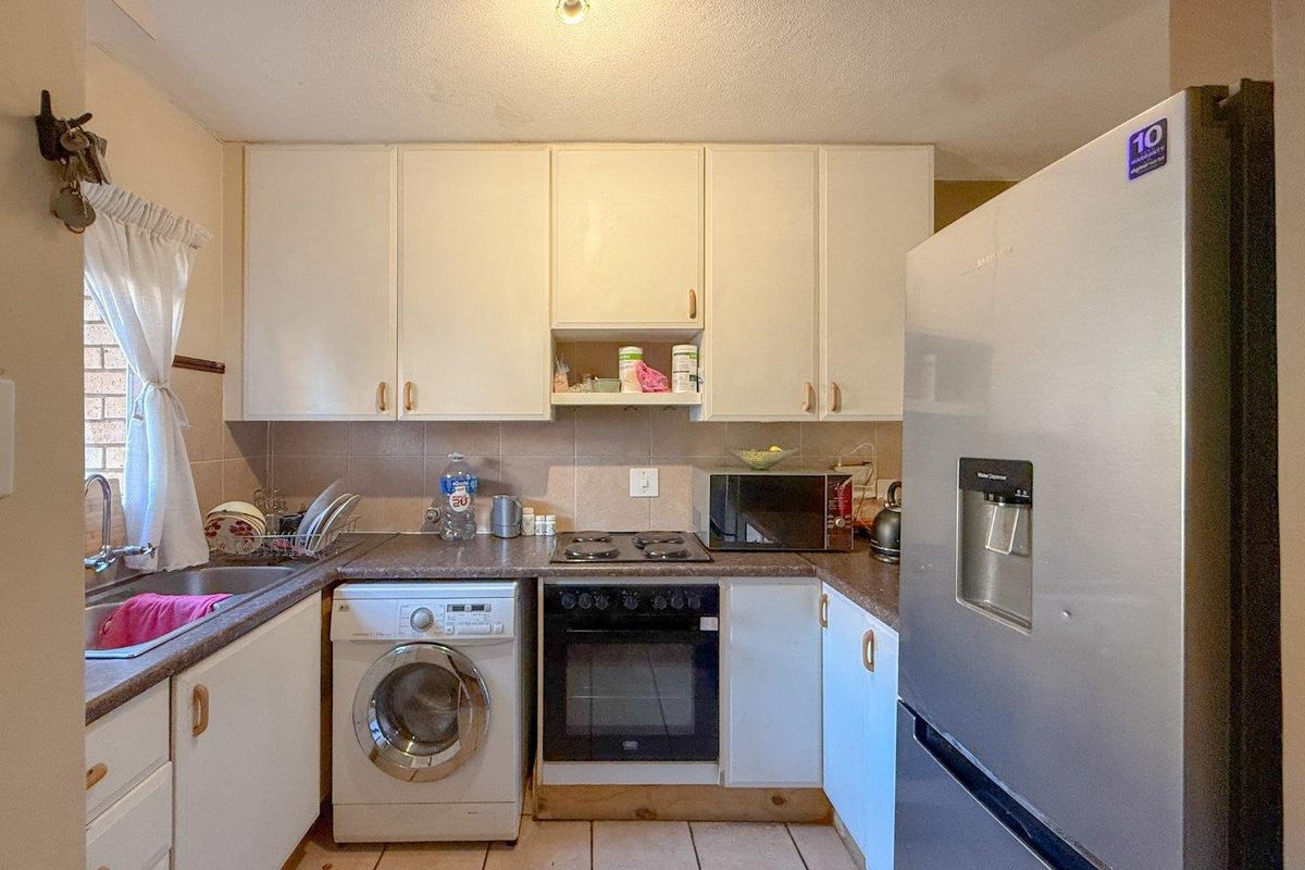 Compact kitchen featuring white cabinetry, laminate countertops, tiled backsplash, and integrated appliances including an oven and hob.
