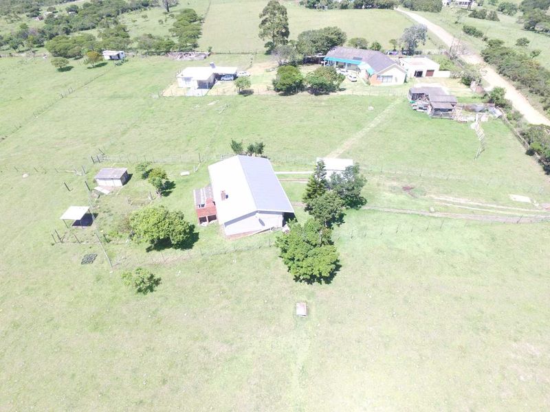 Aerial view of a farm property featuring a main dwelling, multiple outbuildings, fenced paddocks, and surrounding rural landscape.