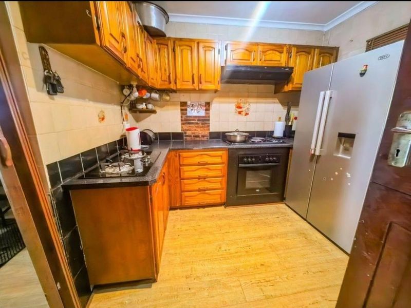 A functional kitchen featuring wooden cabinetry, laminate countertops, a built-in oven, gas hob, and extractor fan with tiled splashbacks.
