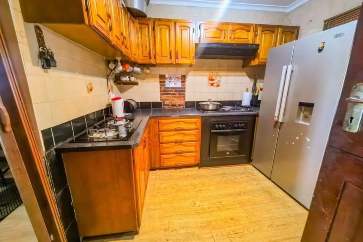 A functional kitchen featuring wooden cabinetry, laminate countertops, a built-in oven, gas hob, and extractor fan with tiled splashbacks.